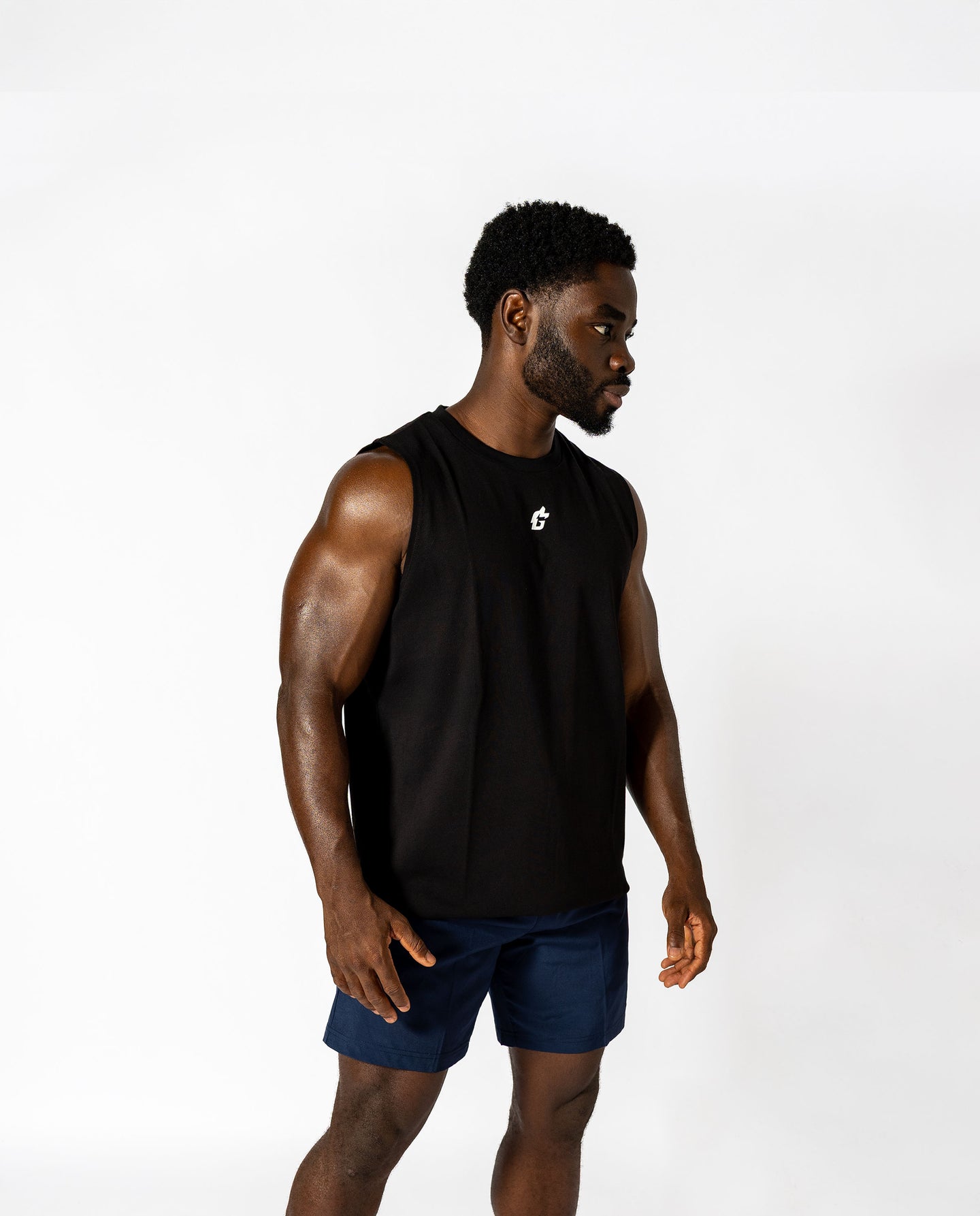 A man in a black tank top and blue shorts, demonstrating a stylish athletic look ideal for lifting and all-day wear.